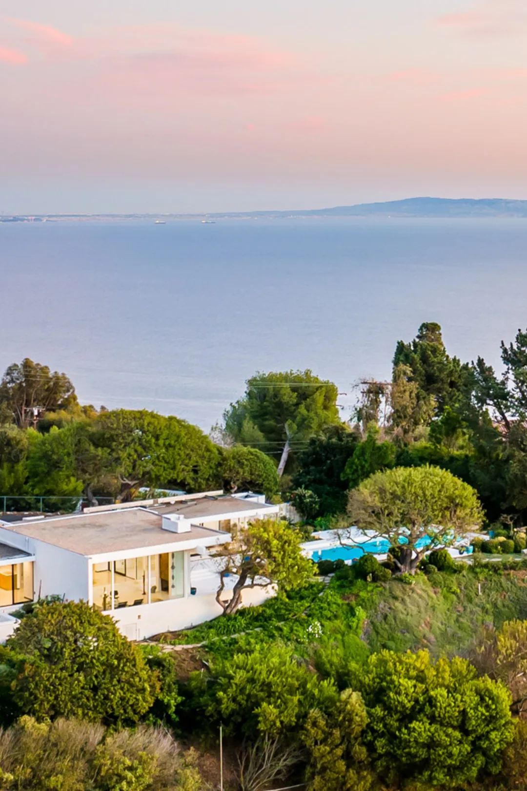A white Modernist house among oaks above the Pacific at dusk.